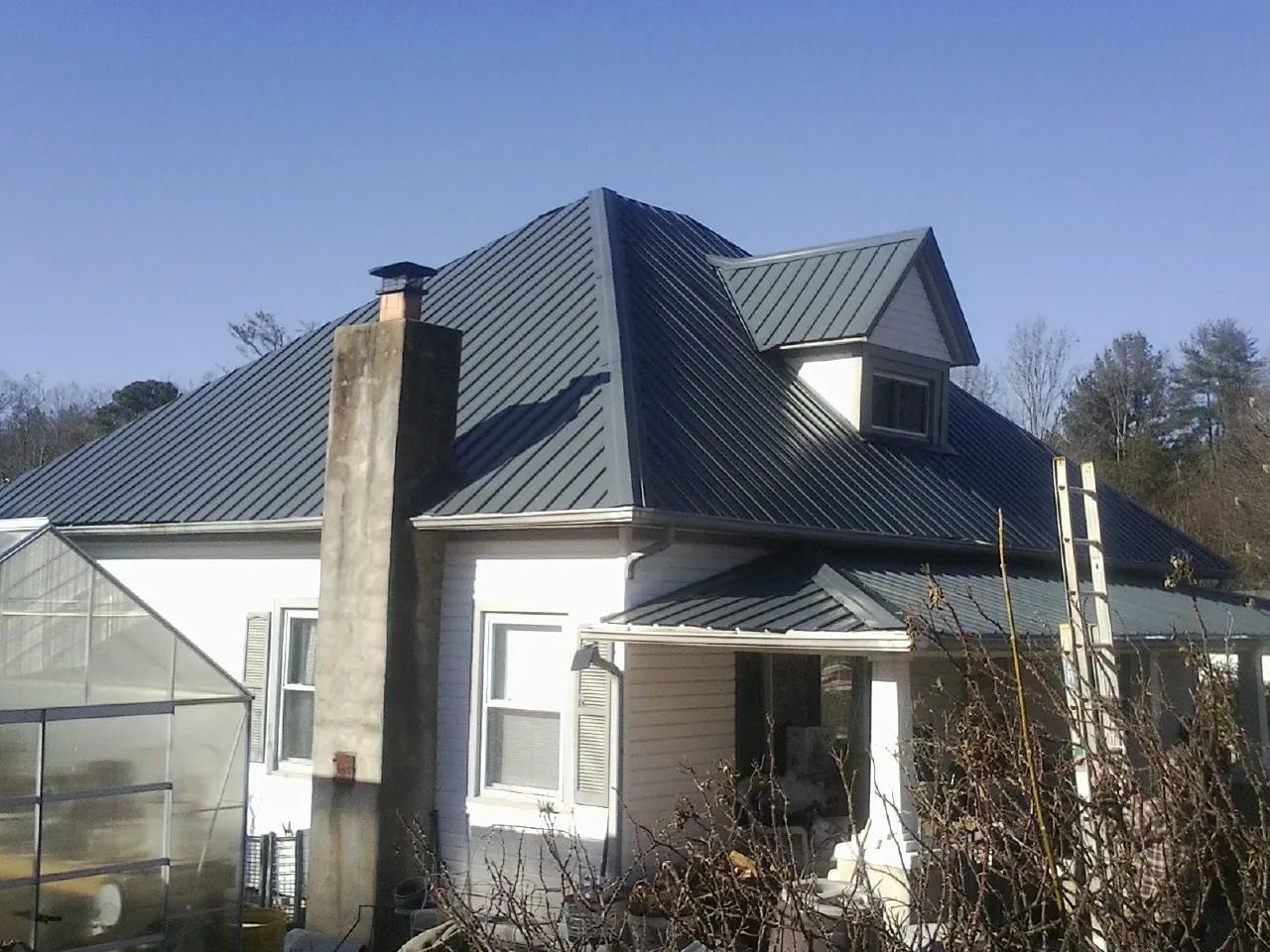 Dark blue standing seam metal roof on a white farmhouse with dormer — Slate & Tile Roof Repair by Roofing Brothers in Luther