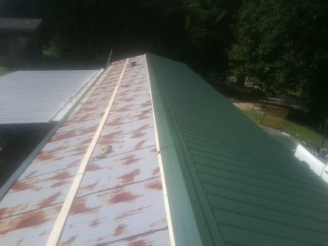 Old rusted panels beside newly installed green metal roofing — Wind Damage Roof Repair by Roofing Brothers in Luther