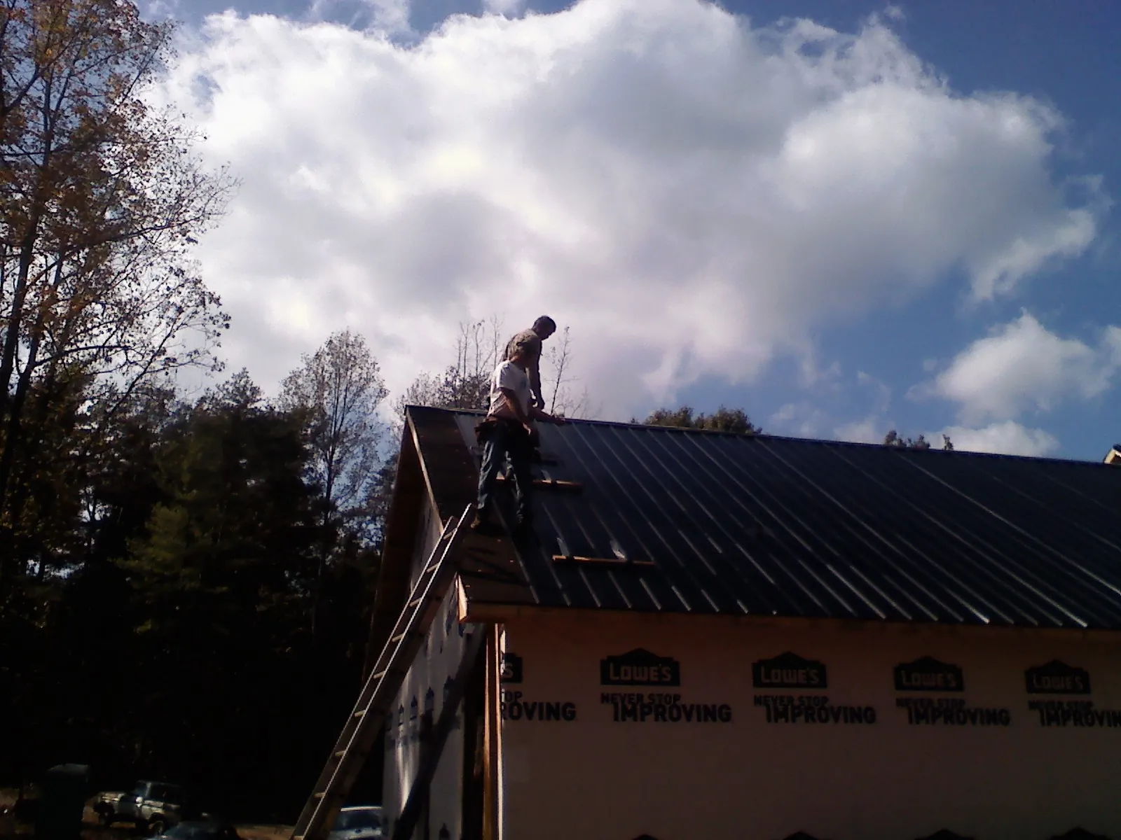 Roofer fastening dark metal panels high against a cloudy sky, from a Roof Inspection job in Luther