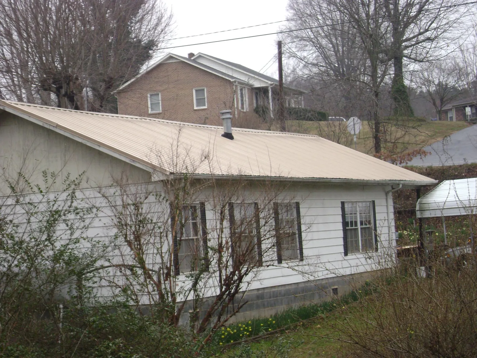 Tan metal roof on a white sided house set into a hillside — Commercial Roofing by Roofing Brothers in Luther