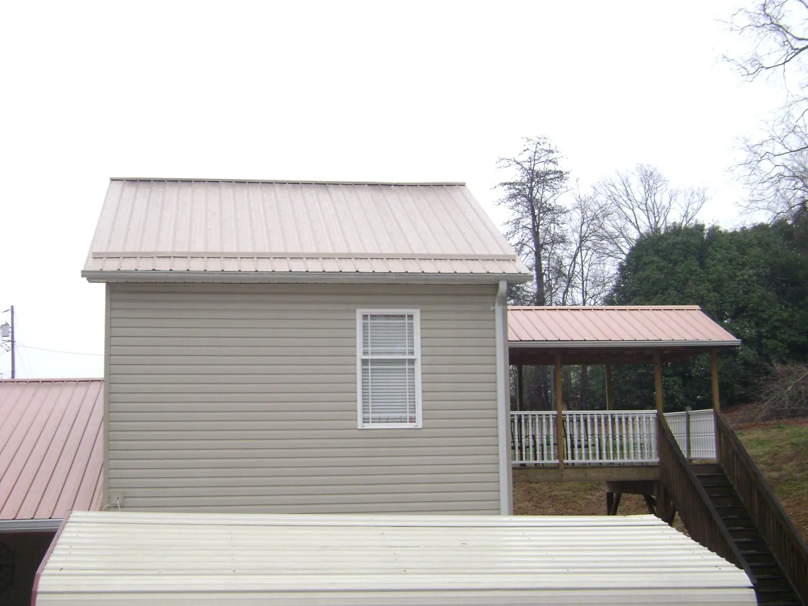 Tan metal roofs on a two story addition and attached porch, from a Roof Replacement job in Luther
